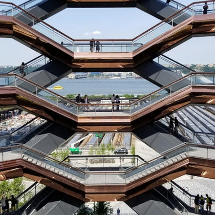 Multi-level structure with people on walkways, river and building in the background, and construction site below.