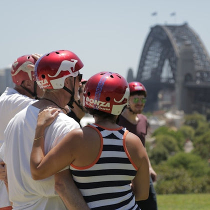 A group of people wearing red helmets with a view of the Sydney Harbour Bridge in the background on a sunny day.