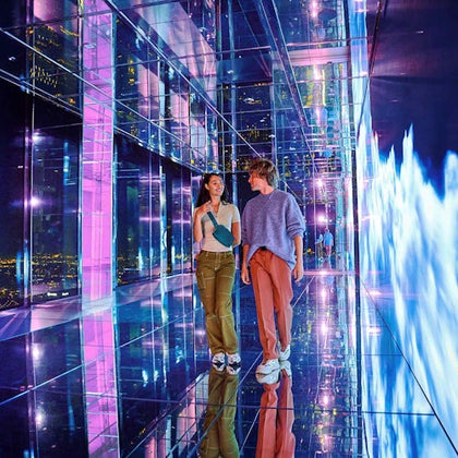 Two people walking through a colorful, mirrored hallway with vibrant lights and a futuristic ambiance.