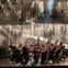 A theatrical performance showing a group of people in dramatic poses on a stage with scaffolding and lighting in the background.