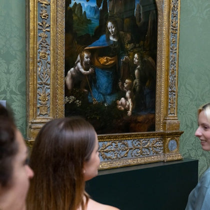 Three people viewing a framed Renaissance painting depicting a woman and children with a naturalistic background in a museum.