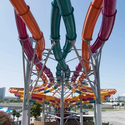 Colorful intertwined water slides viewed from below, with support structures and a sunny outdoor setting in the background.