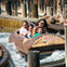 Four people riding a log flume water ride, smiling and enjoying the splash in an amusement park setting.