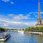 A boat with people floats on a river near the Eiffel Tower on a sunny day, with a bridge and greenery in the background.