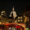 Nighttime cityscape featuring St. Paul's Cathedral dome illuminated, with a red double-decker bus in the foreground.