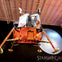 A lunar module replica displayed indoors with a large moon image and the words 'Starship Gallery' in the background.