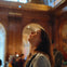 A woman looking upwards in a warmly lit, ornate interior space with arched details and wood paneling.