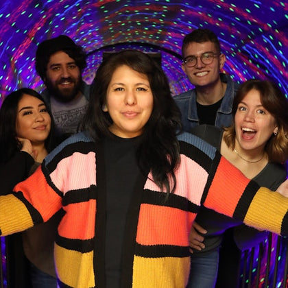 A group of five people smiling and posing in a tunnel with colorful, swirling lights in the background.