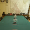 A long table with a green cloth, glasses, and candlesticks in a room with maps, vintage phones, a clock, and a ladder.