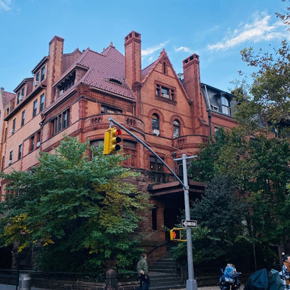 A red brick building with ornate architecture and a steep roof, surrounded by trees, with a streetlight in the foreground.
