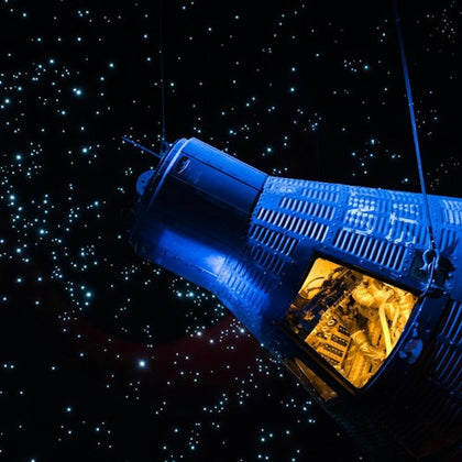 A space capsule suspended in a starry background, with its illuminated interior visible.