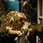 A close-up of a golden lion statue with wings, a halo, and inscriptions on the base, positioned indoors with a dark background.