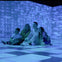 A family of four sits on a checkered floor, smiling and surrounded by blue-lit, abstract digital projections on the walls.