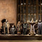 Mannequins dressed in wizard costumes stand on a stage with a large candelabrum in front of tall stained-glass windows.