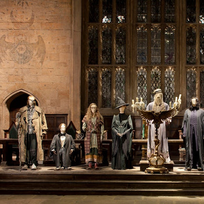 Mannequins dressed in wizard costumes stand on a stage with a large candelabrum in front of tall stained-glass windows.