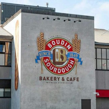 Boudin Sourdough Bakery & Cafe logo painted on a building wall, featuring wheat stalks, text, and a large "B" emblem.