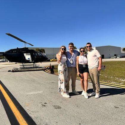 Four people standing in front of a parked black helicopter on an airstrip under a clear blue sky.