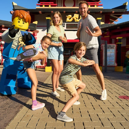 A family poses energetically with a Lego ninja character in front of a building with red and yellow accents.