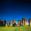 A view of Stonehenge, an ancient stone circle monument, under a clear blue sky with green grass in the foreground.
