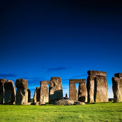 A view of Stonehenge, an ancient stone circle monument, under a clear blue sky with green grass in the foreground.