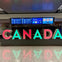 Large, colorful "CANADA" letters in an airport, with flight information screens in the background.