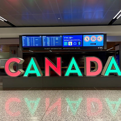 Large, colorful "CANADA" letters in an airport, with flight information screens in the background.