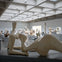 A modern art gallery with various abstract sculptures displayed on pedestals under a grid-patterned ceiling.