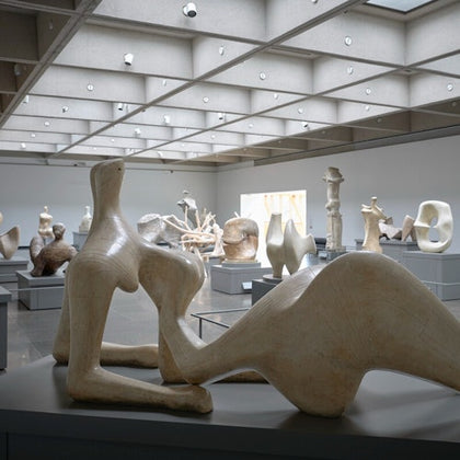 A modern art gallery with various abstract sculptures displayed on pedestals under a grid-patterned ceiling.