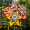 Colorful artistic sculptures of flowers and a bird surrounded by lush tropical plants in a garden setting.