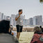 A man stands outside speaking to a small group, with a city skyline in the background.