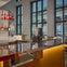 A modern bar area with a glossy counter, liquor bottles on shelves, and large windows revealing a building exterior.
