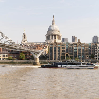 A river scene with a boat labeled 'Uber Boat,' the Millennium Bridge, St. Paul's Cathedral, and city buildings in the background.