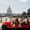 A red golf cart with passengers parked near the U.S. Capitol building on a clear day.