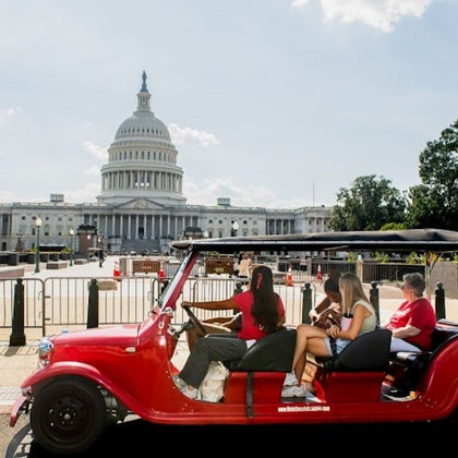 A red golf cart with passengers parked near the U.S. Capitol building on a clear day.
