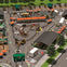 Outdoor activity park featuring construction-themed attractions, vehicles, tracks, and seating areas under orange umbrellas.