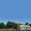 A hilltop with trees and buildings, including a lighthouse, against a clear blue sky.