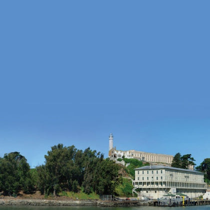 A hilltop with trees and buildings, including a lighthouse, against a clear blue sky.