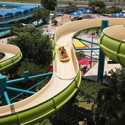 A person riding a yellow tube down a curving water slide at an outdoor water park.