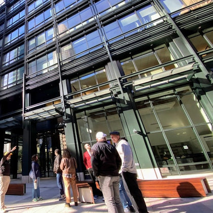 Several people stand talking in front of a modern glass building on a sunny day.