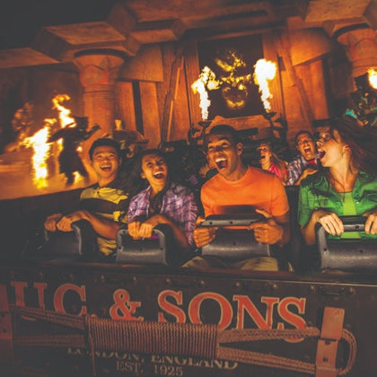 People screaming on a theme park ride with fire, pillars, and a large statue in the background.