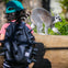 A child with a green cap and spiky black backpack watches a lemur walking along a wooden barrier.