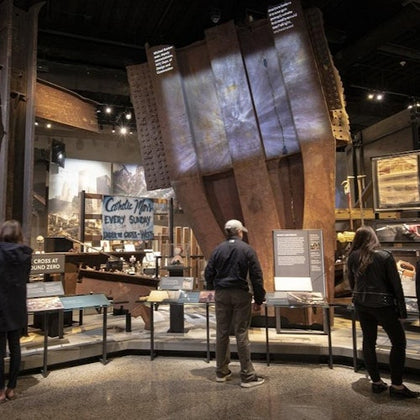 Visitors inside a museum exhibit featuring large steel beams and informational displays about Ground Zero.