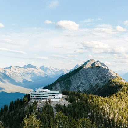 Building on a forested mountain surrounded by distant peaks under a partly cloudy sky.