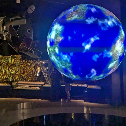 A glowing Earth model and a spacecraft exhibit displayed in a dimly lit science museum setting.