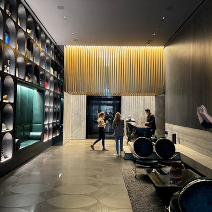 A modern hotel lobby with decorative wall niches, a front desk with staff assisting guests, and sleek furnishings.