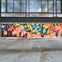 A colorful mural of a reclining figure surrounded by flowers and fruit, set against a modern building with large windows.