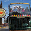A double-decker tour bus with passengers on the top deck near a Fisherman's Wharf sign in San Francisco.