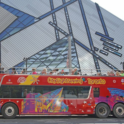 A red double-decker sightseeing bus with the text 'City Sightseeing Toronto,' parked in front of a modern glass building.