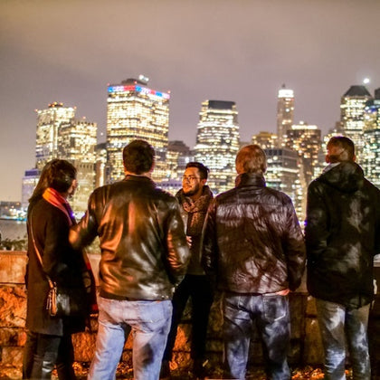 A group of people stand outdoors at night, facing a brightly lit city skyline.