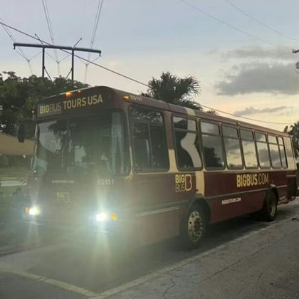 A maroon tour bus with "BIG BUS TOURS USA" and "BIGBUS.COM" branding parked on a street at dusk.